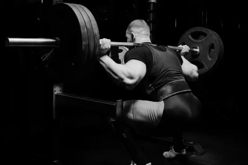 muscular white man in gym with heavy weights on shoulder