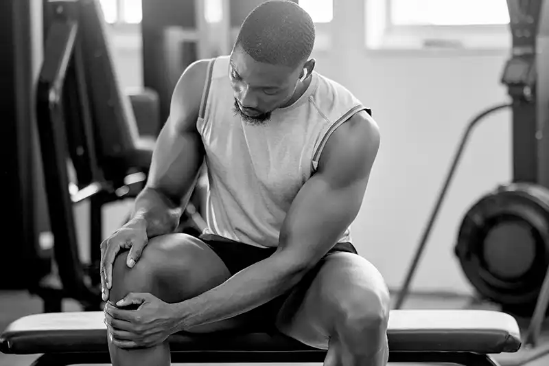 man holding knee sitting on weight bench